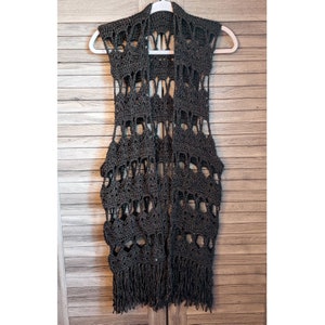May include: Black crochet vest with a fringe hem. The vest has a loose fit and is made of a lightweight material.