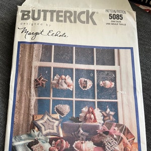 Pode incluir: Um padrão de costura vintage para fazer enfeites de Natal. O padrão é da Butterick e foi desenhado por Margit Echole. O número do padrão é 5085 e é para um único tamanho. O padrão mostra uma variedade de enfeites, incluindo estrelas, anjos, corações e meias. Os enfeites são mostrados em um peitoril de janela com um fundo de madeira.
