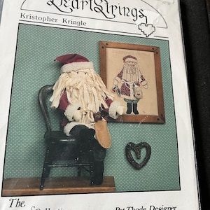 May include: A cross-stitch pattern for a Santa Claus doll, titled "Kristopher Kringle" by Pat Thod, designer. The pattern is from the "The Artists Collection" series by HeartStrings.