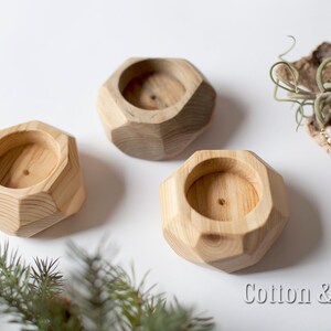 May include: Three wooden candle holders with a geometric design. The holders are made of light brown wood and have a smooth finish. The holders are arranged in a row on a white surface. The text "Cotton & Wood design" is visible in the bottom right corner of the image.