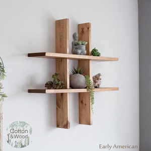 May include: A wooden shelf unit with a criss-cross design. The shelf is made of natural wood and has three shelves. The shelves are decorated with small plants and a small statue. The text "Early American" is visible at the bottom of the image.