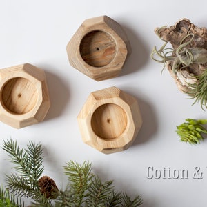 May include: Three wooden candle holders with a geometric design. The holders are made of natural wood and have a light brown color. The holders are arranged in a triangular pattern on a white surface.