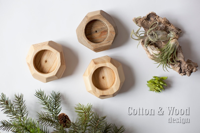 May include: Three wooden candle holders with a geometric design. The holders are made of natural wood and have a light brown color. The holders are arranged in a triangular pattern on a white surface.