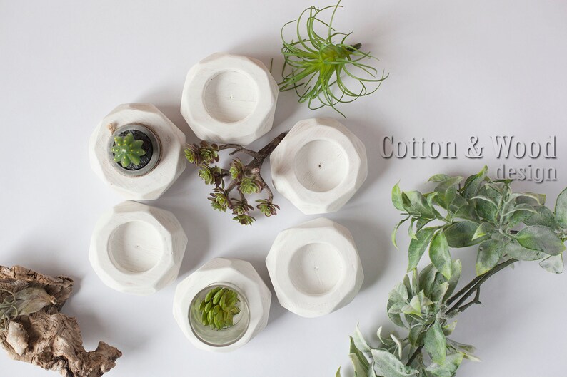 May include: Six white geometric concrete candle holders with a small succulent plant in one of the holders. The holders are arranged in a circle on a white surface. The text "Cotton & Wood design" is visible in the upper right corner of the image.
