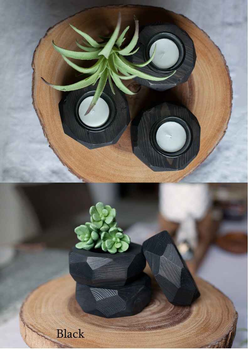May include: Three black wooden candle holders with a geometric design. The candle holders are on a wooden slice. The candle holders are filled with white tea lights. A small green succulent plant is in the center of the wooden slice.