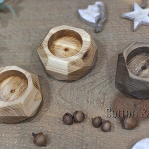 May include: Three wooden candle holders with geometric shapes. The candle holders are made of natural wood with a light brown and dark brown finish. The candle holders are arranged on a wooden surface. The text "Cotton & Wood design" is visible in the bottom right corner of the image.