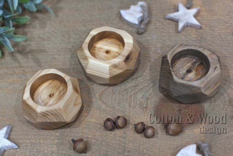 May include: Three wooden candle holders with geometric shapes. The candle holders are made of natural wood with a light brown and dark brown finish. The candle holders are arranged on a wooden surface. The text "Cotton & Wood design" is visible in the bottom right corner of the image.