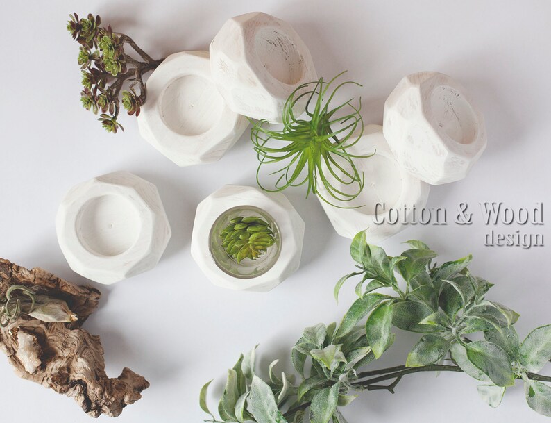 May include: White geometric candle holders with a textured finish. The holders are arranged on a white surface with green plants.