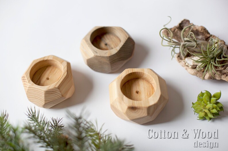 May include: Three wooden candle holders with a geometric design. The holders are made of light brown wood and have a smooth finish. The holders are arranged in a row on a white surface. The text "Cotton & Wood design" is visible in the bottom right corner of the image.