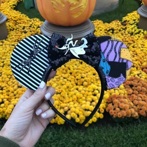 May include: Black and white striped Minnie Mouse ears with a black bow and a white and purple patchwork ear. The bow features a white silhouette of Jack Skellington from The Nightmare Before Christmas.