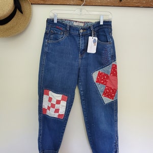 May include: Blue denim jeans with red and white patchwork on the knees and right thigh. The patchwork is in a checkered and floral pattern.