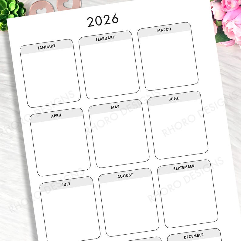 May include: A white 2026 yearly calendar planner page featuring a grid layout with twelve rounded rectangular boxes for each month from January to December. Each month header is displayed in black text on a light gray background bar.