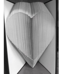 Puede incluir: Imagen en blanco y negro de una escultura en forma de corazón hecha con las páginas de un libro. Las páginas están dobladas y dispuestas para formar la forma del corazón, con los bordes de las páginas visibles.