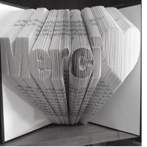 Puede incluir: Una escultura de arte de libro de la palabra "MERGE" creada doblando las páginas de un libro. Las páginas están dobladas para crear un efecto 3D.