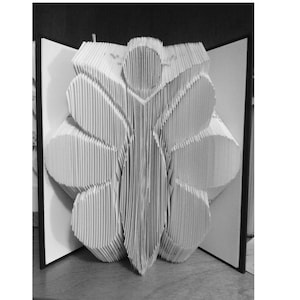 Puede incluir: Escultura de papel en blanco y negro de una flor o mariposa. La obra de arte se crea doblando y organizando numerosas páginas de papel para formar un diseño tridimensional. La escultura se exhibe dentro de un libro abierto.