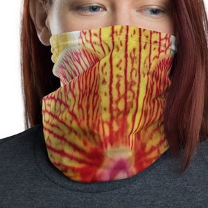 May include: A face covering with a vibrant floral design. The fabric features a close-up of a yellow and red flower, with vertical red lines against a yellow background. The face covering is worn by a person with red hair and a gray shirt.