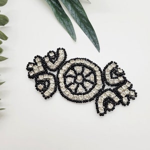 May include: A black and white beaded embellishment with a circular design and floral accents. The embellishment is made of small black beads and clear rhinestones.