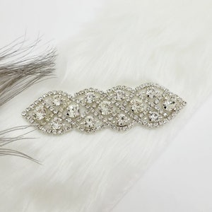 May include: A silver rhinestone trim with a wavy design. The trim is made of small, clear rhinestones set in a silver metal base.