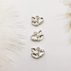 May include: Three crystal embellishments in the shape of a flower with a single round crystal in the center of each flower.