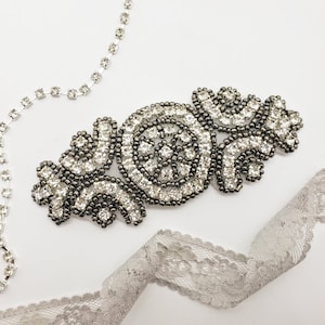May include: A silver rhinestone embellishment with a floral design. The embellishment is made of small, round rhinestones that are set in a silver metal base.