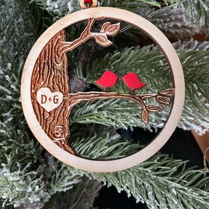 K&ouml;nnte beinhalten: Ein h&ouml;lzerner Weihnachtsbaumschmuck mit einem Baum und zwei roten V&ouml;geln. Der Schmuck hat ein Herz mit den Initialen "D+G" eingraviert.