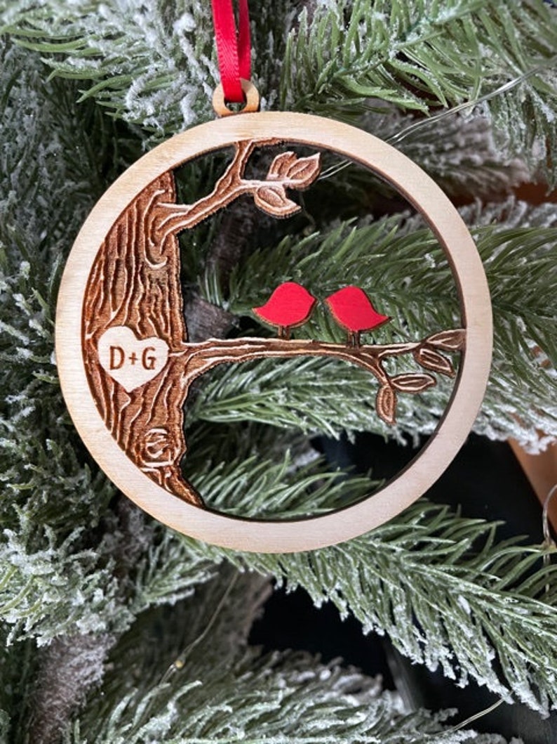 K&ouml;nnte beinhalten: Ein h&ouml;lzerner Weihnachtsbaumschmuck mit einem Baum und zwei roten V&ouml;geln. Der Schmuck hat ein Herz mit den Initialen "D+G" eingraviert.