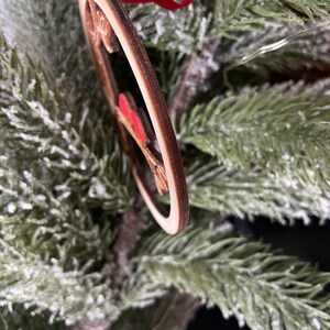 K&ouml;nnte beinhalten: Ein h&ouml;lzerner Weihnachtsbaumschmuck in Herzform mit einem roten Band. Der Schmuck ist mit einem roten und wei&szlig;en Muster verziert.
