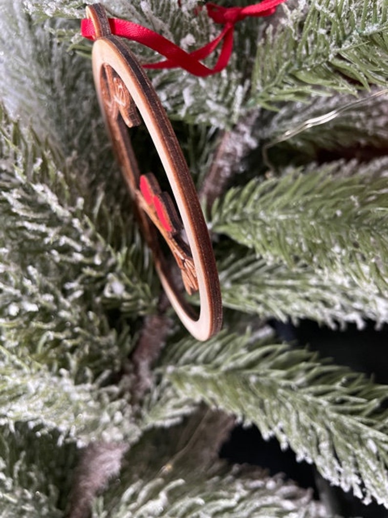 K&ouml;nnte beinhalten: Ein h&ouml;lzerner Weihnachtsbaumschmuck in Herzform mit einem roten Band. Der Schmuck ist mit einem roten und wei&szlig;en Muster verziert.