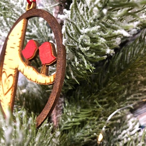 K&ouml;nnte beinhalten: Ein h&ouml;lzerner Weihnachtsbaumschmuck in Form eines Halbmondes mit zwei roten V&ouml;geln, die auf einem Ast sitzen. Der Schmuck h&auml;ngt an einem verschneiten k&uuml;nstlichen Weihnachtsbaum.