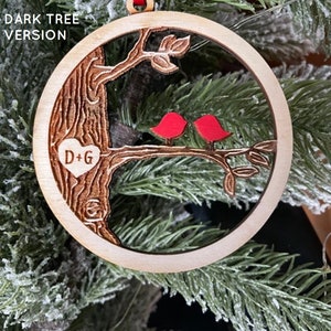 K&ouml;nnte beinhalten: Ein h&ouml;lzerner Weihnachtsbaumschmuck mit einem geschnitzten Baum, zwei roten V&ouml;geln und den Initialen "D+G" in einem Herzen. Der Schmuck h&auml;ngt an einem Weihnachtsbaum.