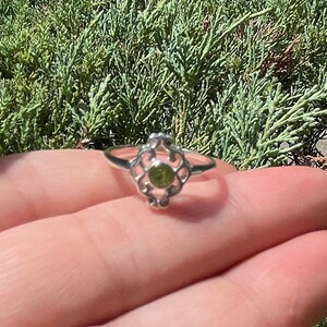 Può includere: Un anello d'argento con una pietra preziosa verde incastonata in un design a filigrana decorativo.