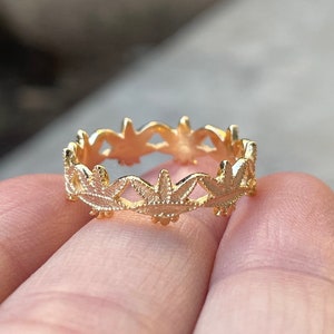 May include: A gold ring with a delicate design of leaves around the band.