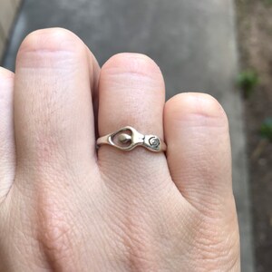 Peut inclure: Une bague en argent au design unique, avec un &eacute;l&eacute;ment en forme de c&oelig;ur et un petit d&eacute;tail en spirale. La bague est port&eacute;e au doigt, mettant en valeur son artisanat d&eacute;licat et son style minimaliste.