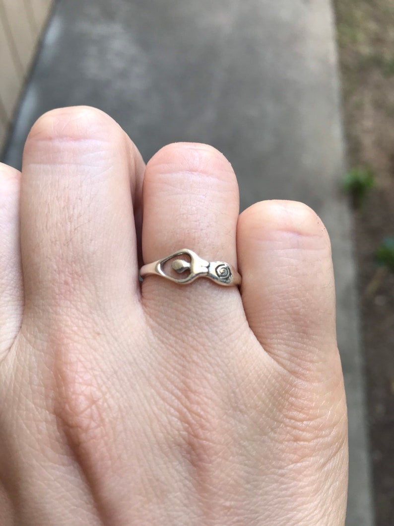 Peut inclure: Une bague en argent au design unique, avec un &eacute;l&eacute;ment en forme de c&oelig;ur et un petit d&eacute;tail en spirale. La bague est port&eacute;e au doigt, mettant en valeur son artisanat d&eacute;licat et son style minimaliste.