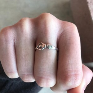 Peut inclure: Une bague en argent au design unique, avec une forme de goutte d'eau centrale et un petit symbole stylis&eacute; sur le bandeau. La bague est port&eacute;e au doigt, mettant en valeur ses d&eacute;tails complexes et sa finition polie.