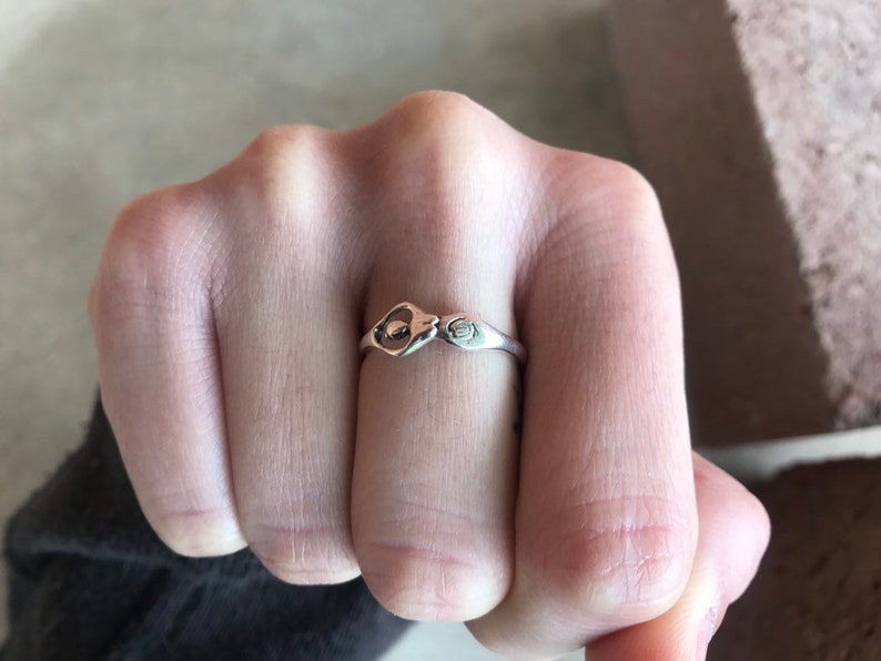 Peut inclure: Une bague en argent au design unique, avec une forme de goutte d'eau centrale et un petit symbole stylis&eacute; sur le bandeau. La bague est port&eacute;e au doigt, mettant en valeur ses d&eacute;tails complexes et sa finition polie.