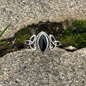 May include: A silver ring with a black onyx stone set in a Celtic knot design.