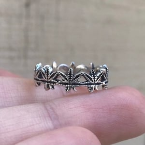 May include: A silver ring with a detailed design of leaves around the band.