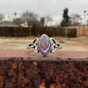 May include: A silver ring with a purple amethyst gemstone set in a Celtic knot design.