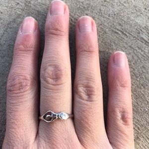 Peut inclure: Une bague en argent avec un motif de calla. La bague a un anneau fin et un motif floral d&eacute;taill&eacute;, repr&eacute;sentant un calla et un petit accent. La bague est pr&eacute;sent&eacute;e sur une main.