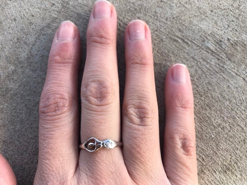 Peut inclure: Une bague en argent avec un motif de calla. La bague a un anneau fin et un motif floral d&eacute;taill&eacute;, repr&eacute;sentant un calla et un petit accent. La bague est pr&eacute;sent&eacute;e sur une main.