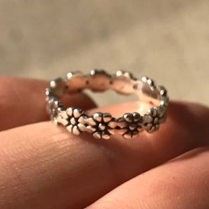 May include: A silver ring with a delicate floral design. The ring is made of a thin band and features a series of small, raised flowers.
