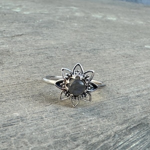 Puede incluir: Un anillo de plata con una piedra preciosa gris engastada en un diseño con forma de flor.