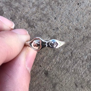 Peut inclure: Une bague en argent au design d&eacute;licat. La bague pr&eacute;sente un motif floral stylis&eacute; et un motif ajour&eacute; central. La bague est tenue par les doigts d'une personne. La bague est probablement en argent sterling.