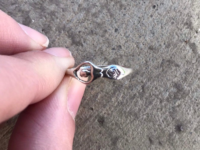 Peut inclure: Une bague en argent au design d&eacute;licat. La bague pr&eacute;sente un motif floral stylis&eacute; et un motif ajour&eacute; central. La bague est tenue par les doigts d'une personne. La bague est probablement en argent sterling.