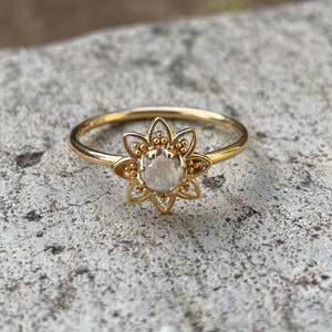 Puede incluir: Un anillo de oro con un delicado diseño floral y una piedra preciosa transparente en el centro.