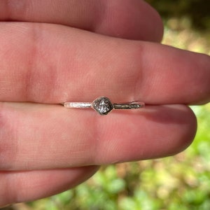 May include: A silver ring with a small, clear gemstone set in a textured band.
