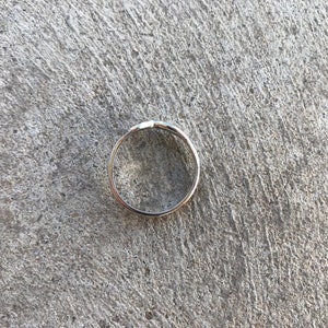 Peut inclure: Une bague en argent au design simple et &eacute;l&eacute;gant. La bague est circulaire avec un petit d&eacute;tail en relief sur le dessus. La bague est pos&eacute;e sur une surface en b&eacute;ton grise textur&eacute;e.