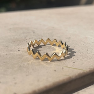 May include: A gold-colored ring with a zig-zag pattern around the band.