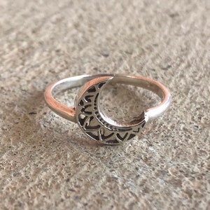 May include: A silver ring with a crescent moon design. The moon is detailed with intricate cutouts.